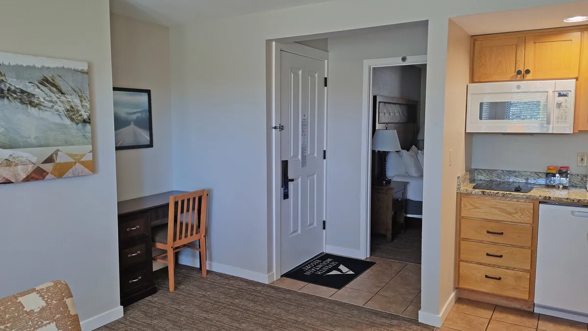 A cozy interior featuring a compact kitchenette, a desk with a chair, framed artwork, and views into the bedroom. The space feels casual and comfortable, with amenities ideal for preparing easy meals and enjoying downtime after a day of outdoor activities.