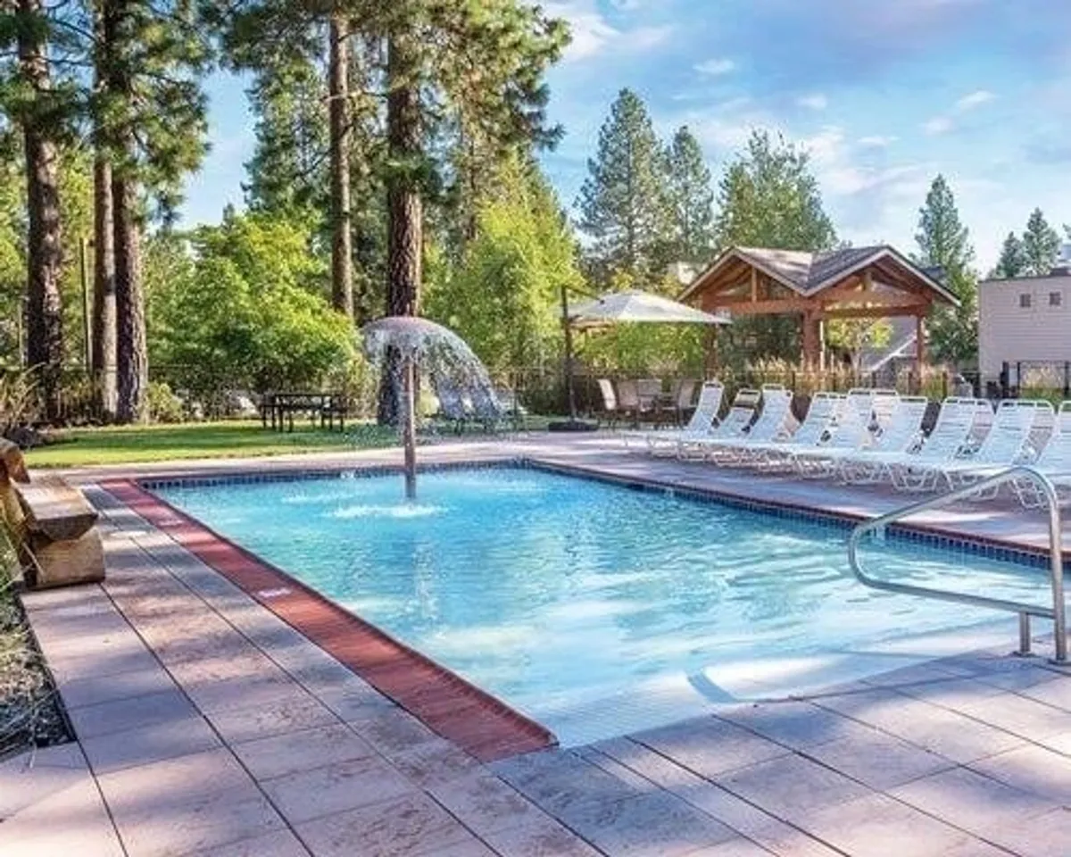 This image showcases a large swimming pool surrounded by trees, with lounge chairs and a gazebo, creating a tranquil and inviting outdoor setting. The pool is central, with a fountain adding a refreshing touch, and the area is clearly designed for both relaxation and social gatherings.