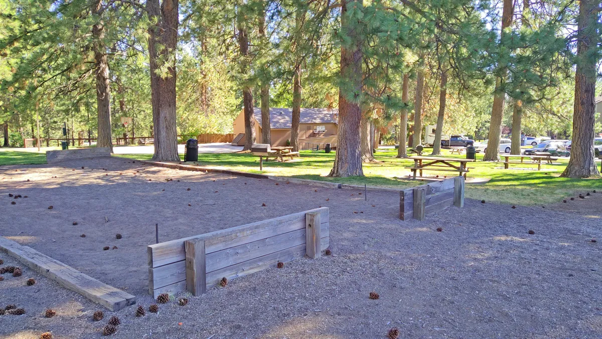 A playful outdoor area featuring a sandbox, picnic tables, and mature trees. The setting suggests family gatherings, relaxation, and opportunities for casual outdoor fun close to nature.