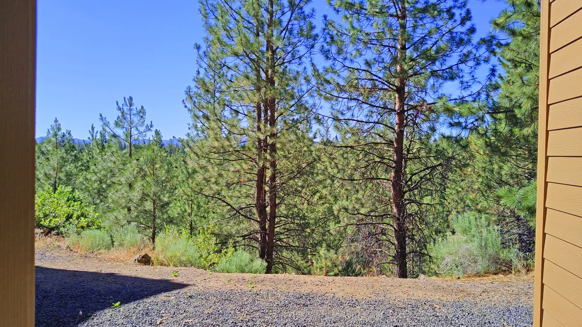 This image features a scenic view of tall pine trees, distant mountains, and a clear blue sky. The natural beauty visible from the property connects the balcony experience to the broader landscape of Central Oregon.