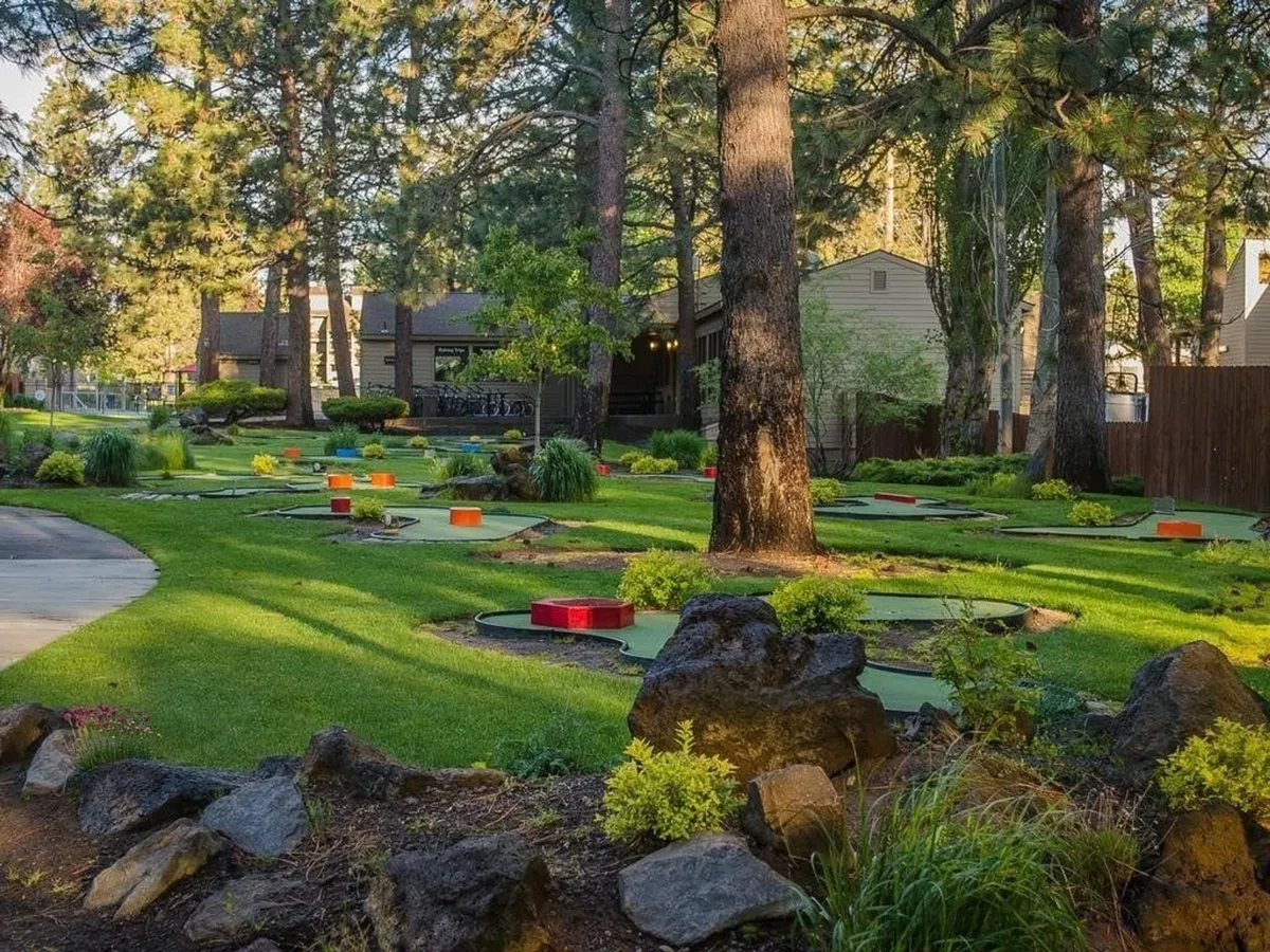This image features a vibrant mini-golf course with colorful obstacles, surrounded by lush greenery and tall trees. A walkway winds through the space, suggesting easy access for guests of all ages to engage in friendly competition or leisurely walks.