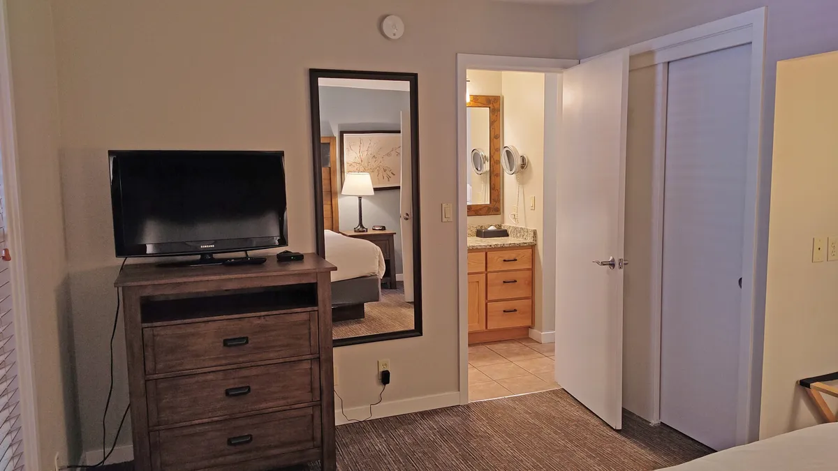 A cozy living space featuring a television, dresser, and a mirror, with a soft glow from natural lighting. The bathroom door is visible, suggesting easy transition from relaxation to getting ready for outdoor adventures. The room invites guests to unwind, watch a movie, or prepare for the day's activities.
